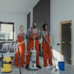 Diverse cleaning team in red uniforms ready to sanitize a modern living room with vacuum and mop.